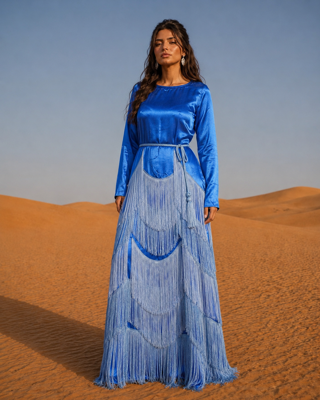 Woman in a blue dress with fringe standing in a desert landscape