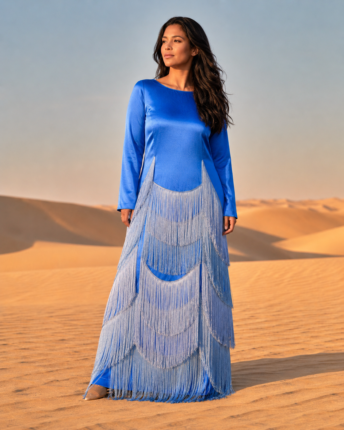 Woman in a blue dress with fringe standing in a desert landscape