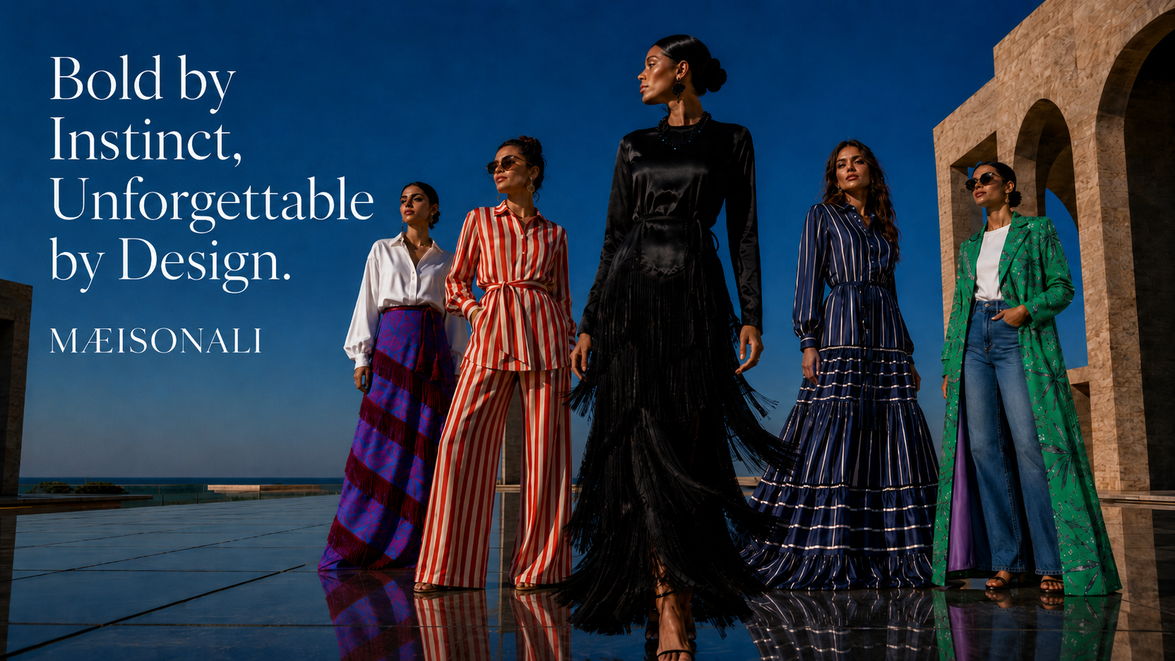 Five models in M.Eisonali clothing standing against a blue sky with ocean view.